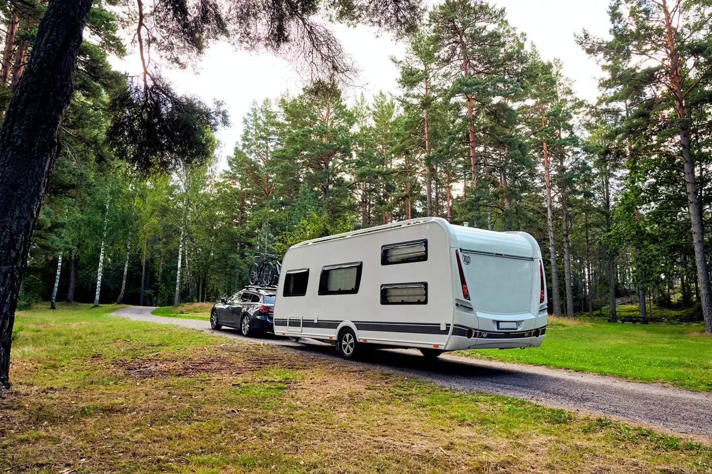 Caravane tractée par une voiture sur un chemin forestier